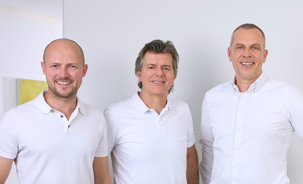 Die drei Ärzte der Gemeinschaftspraxis nebeneinander vor heller Wand